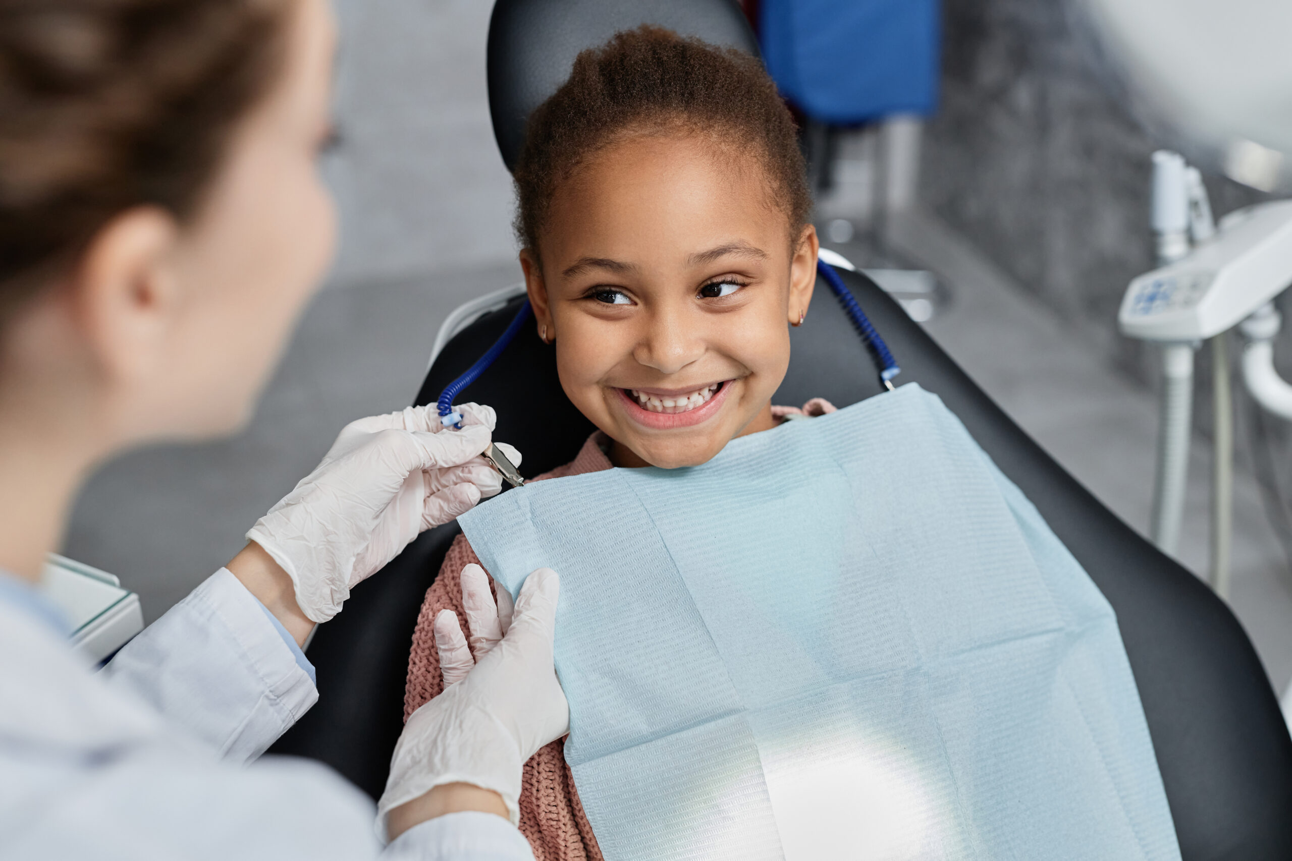 Pediatric Dentistry Portrait of smiling little girl in dental chair with nurse preparing her for teeth check up, copy space